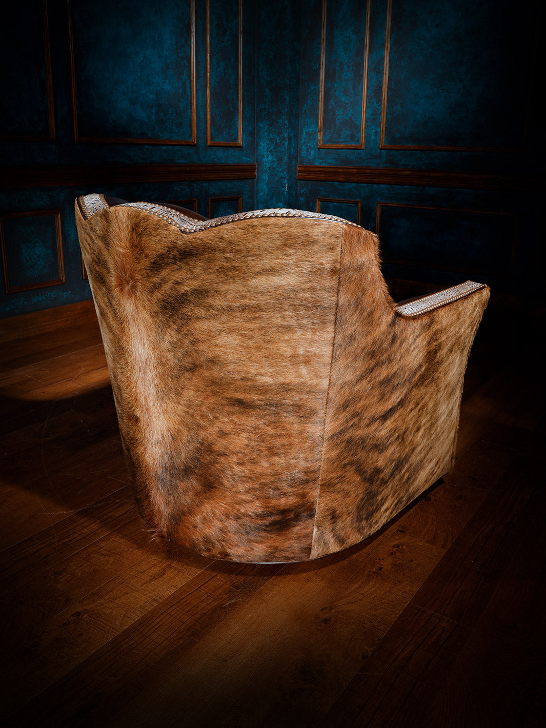 Back view of a western-style swivel chair fully upholstered in hair-on-hide with detailed nailhead trim along the edges.