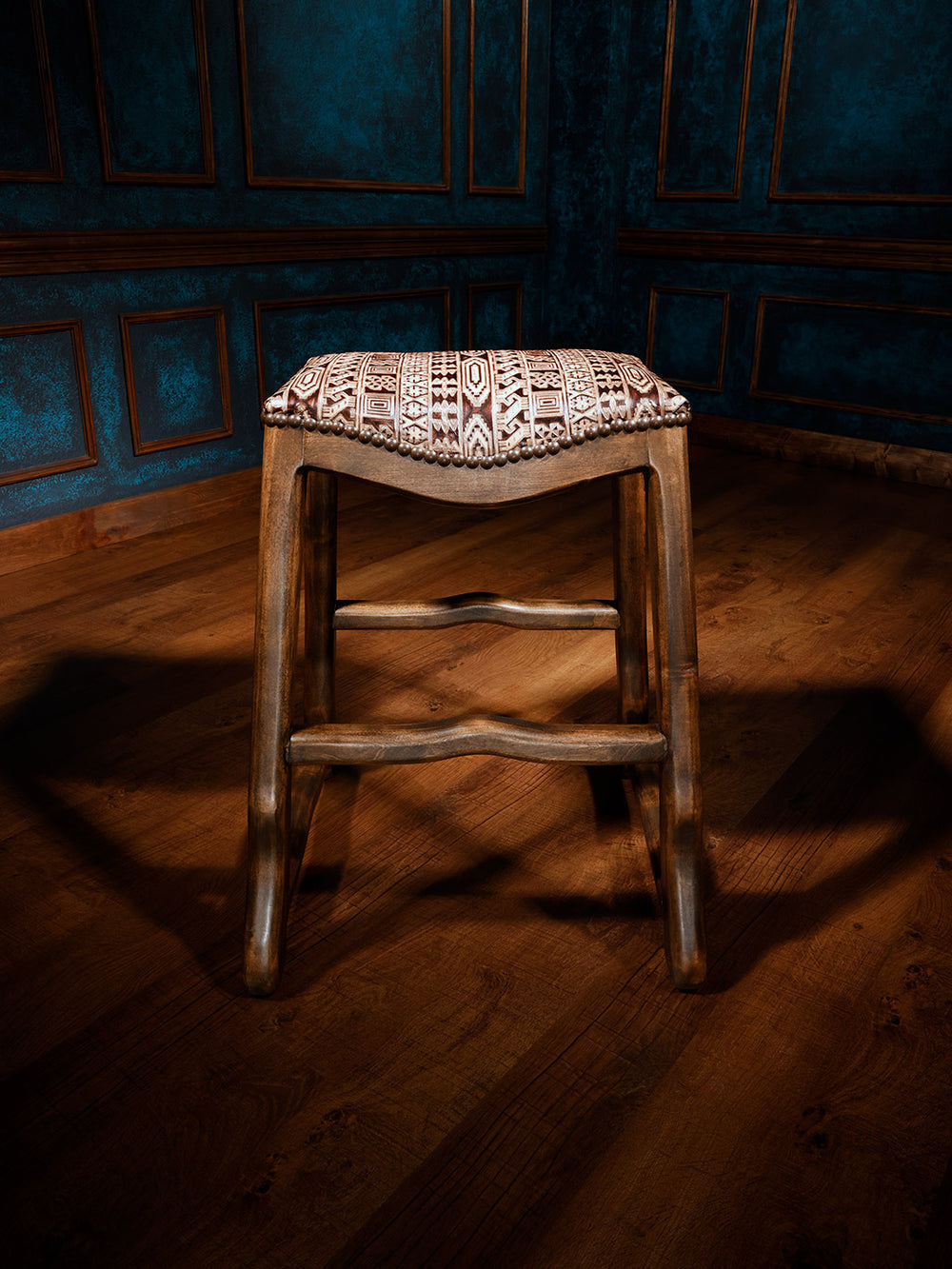 a western saddle stool featuring a tooled leather seat with intricate western patterns, accented with nailhead trim and sturdy wooden legs, front view