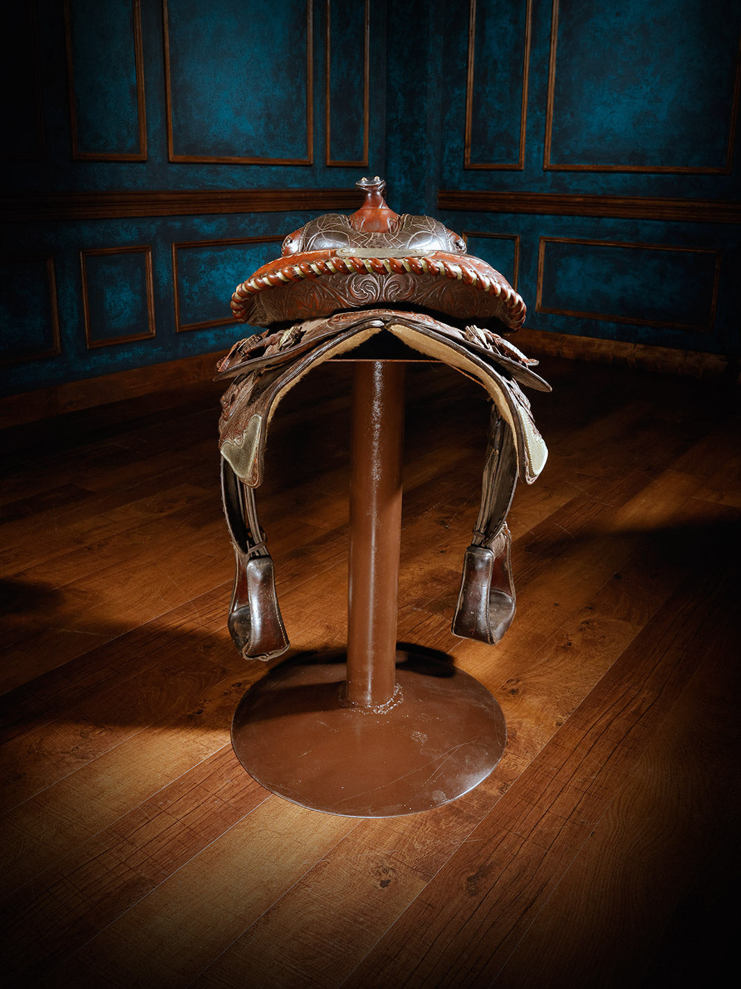 A unique bar stool designed with a richly tooled leather Western saddle, mounted on a sturdy metal base, offering a rustic and authentic cowboy aesthetic.