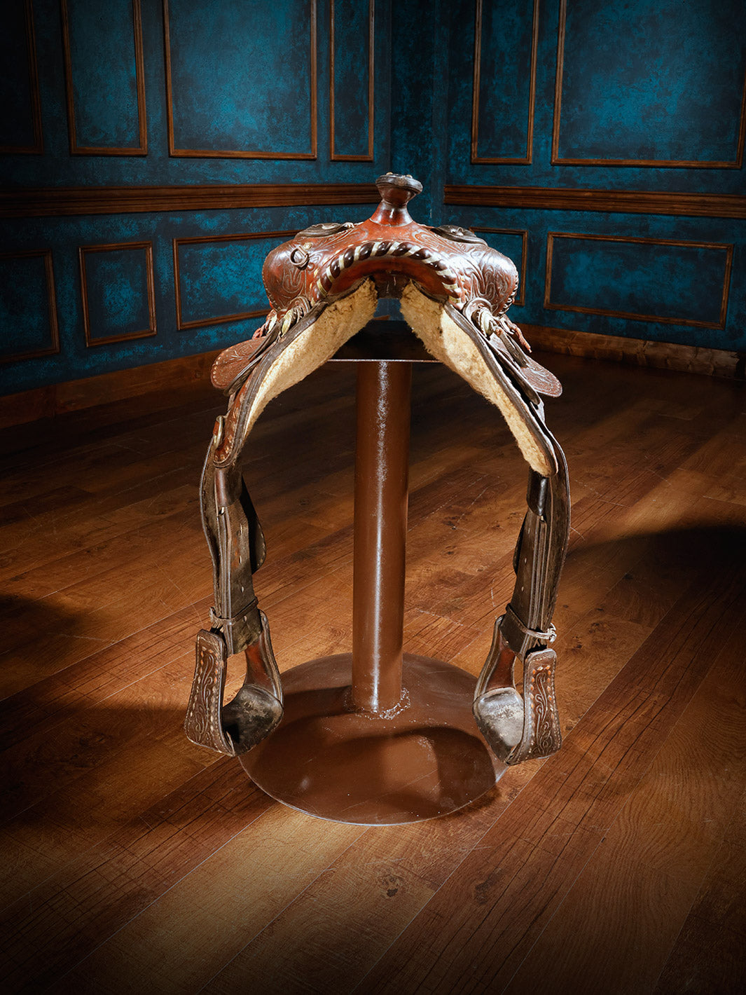 A unique bar stool designed with a richly tooled leather Western saddle, mounted on a sturdy metal base, offering a rustic and authentic cowboy aesthetic.