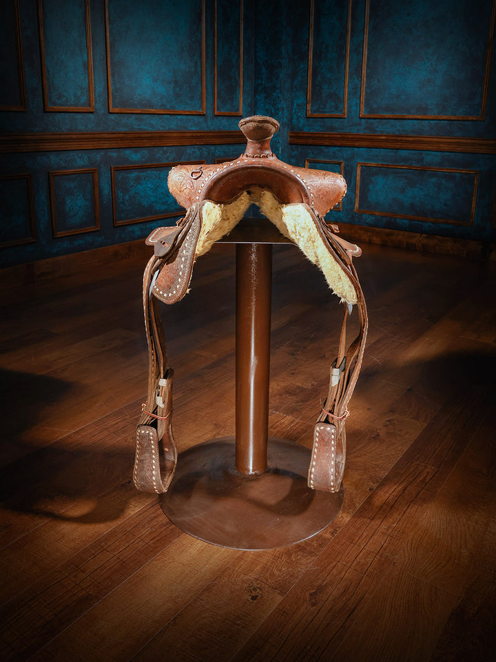 front view of a western-style saddle bar stool, showcasing the underside with plush fleece lining and durable stirrups, mounted on a metal base.